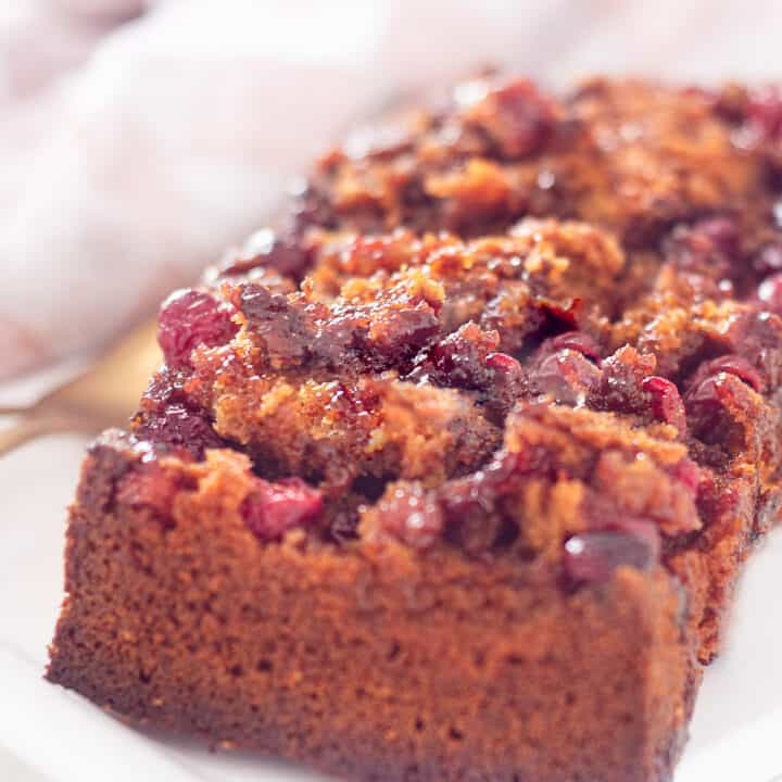 Op een wit schaaltje ligt een cake met cranberry topping en twee kopjes met koffie