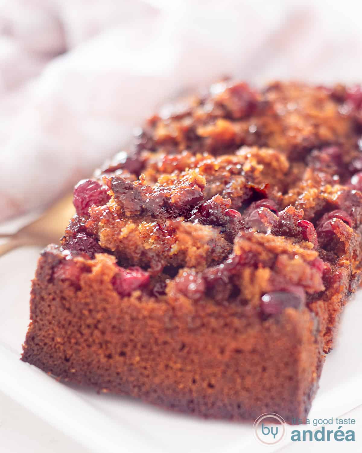 Op een wit schaaltje ligt een cake met cranberry topping en twee kopjes met koffie