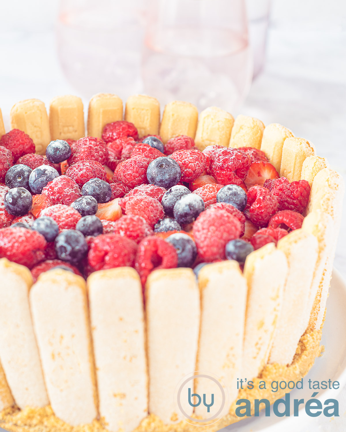 Een deel van een charlotte russe met lange vingers en zomerfruit op een witte achtergrond. Met aardbeien, frambozen en blauwe bessen