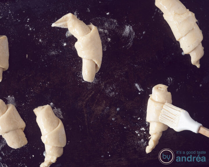 Croissants op een zwarte bakplaat, ingesmeerd met ei.