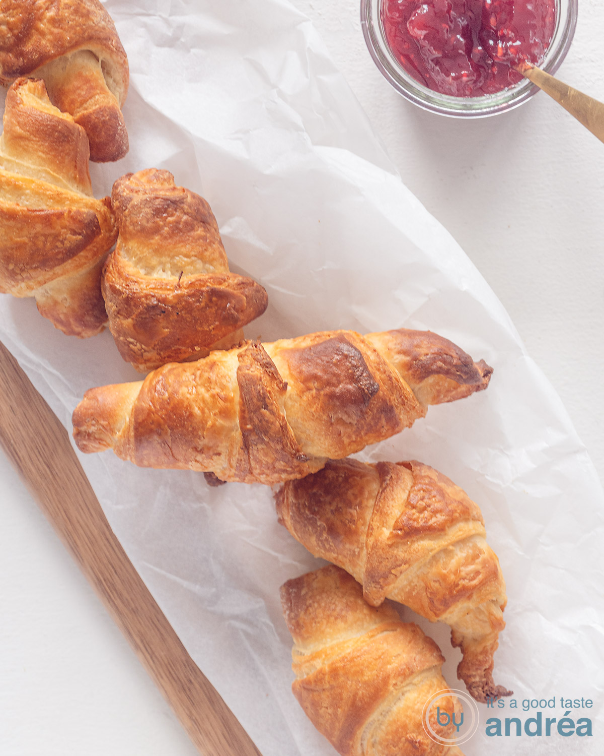 Een foto van bovenaf van een rij croissants op een bakpapier op een plank