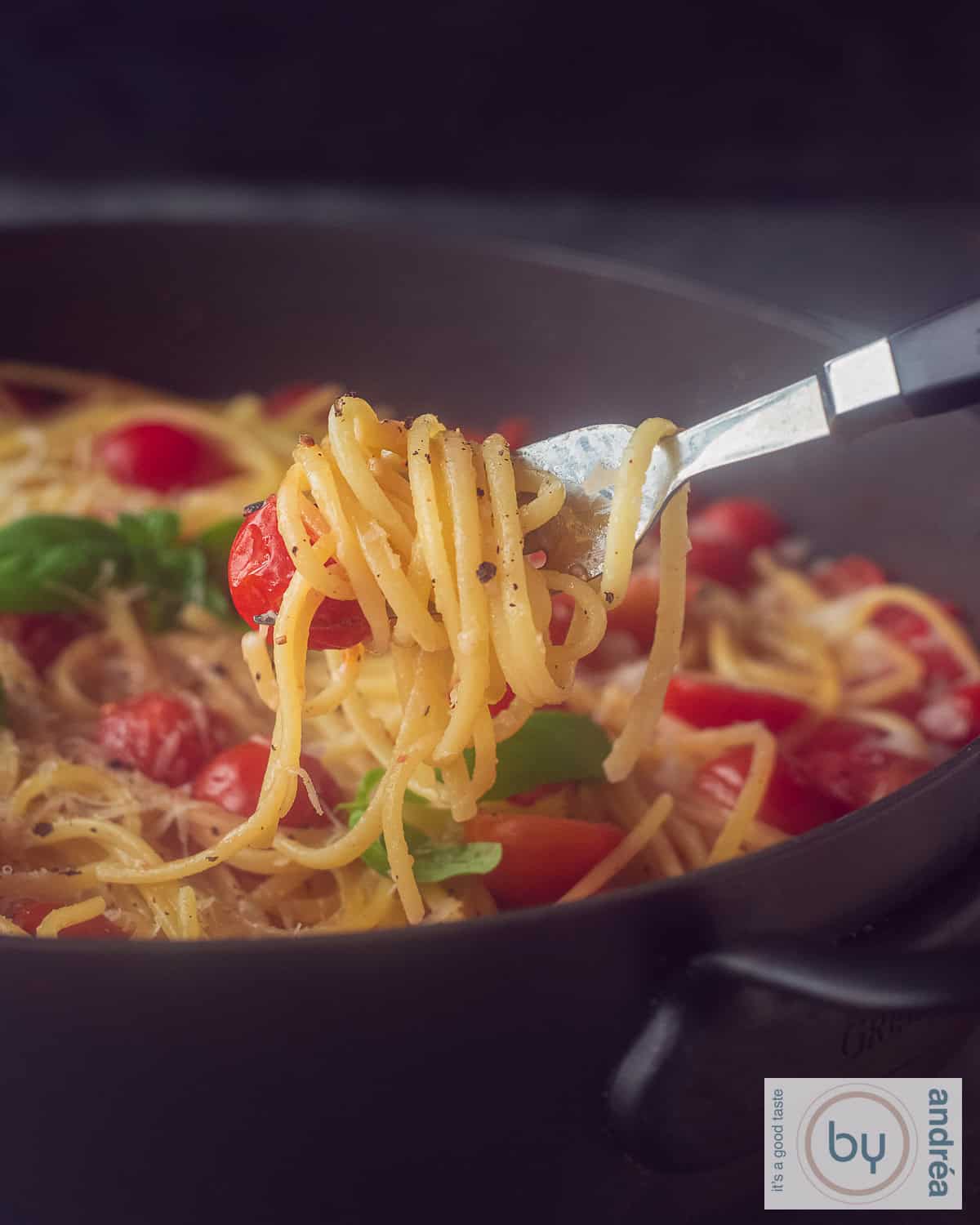 Een foto van bovenaf met pasta, basilicum, ui, kaas en cherry tomaten op een witte ondergrond. Een vork prikt in de linguine.