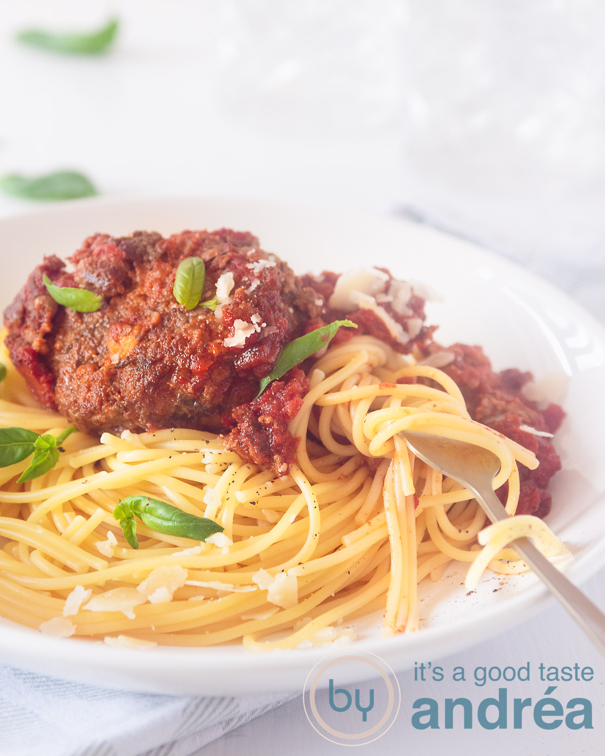 Een deel van een wit bord met spaghetti en gehaktballen in tomatnesaus met Parmezaanse kaas en salie. Spaghetti om een gouden vork gedraaid. Een witte achtergrond.