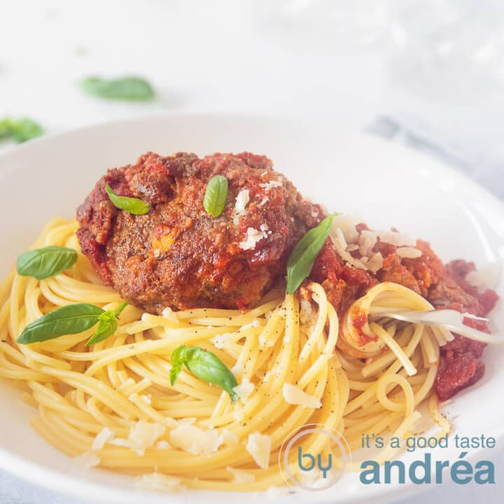 Een vierkante foto met een wit diep bord gevuld met spaghetti tomatensaus en smaakvolle gehaktballen met salie en Parmezaanse kaas. Een witte achtergrond.