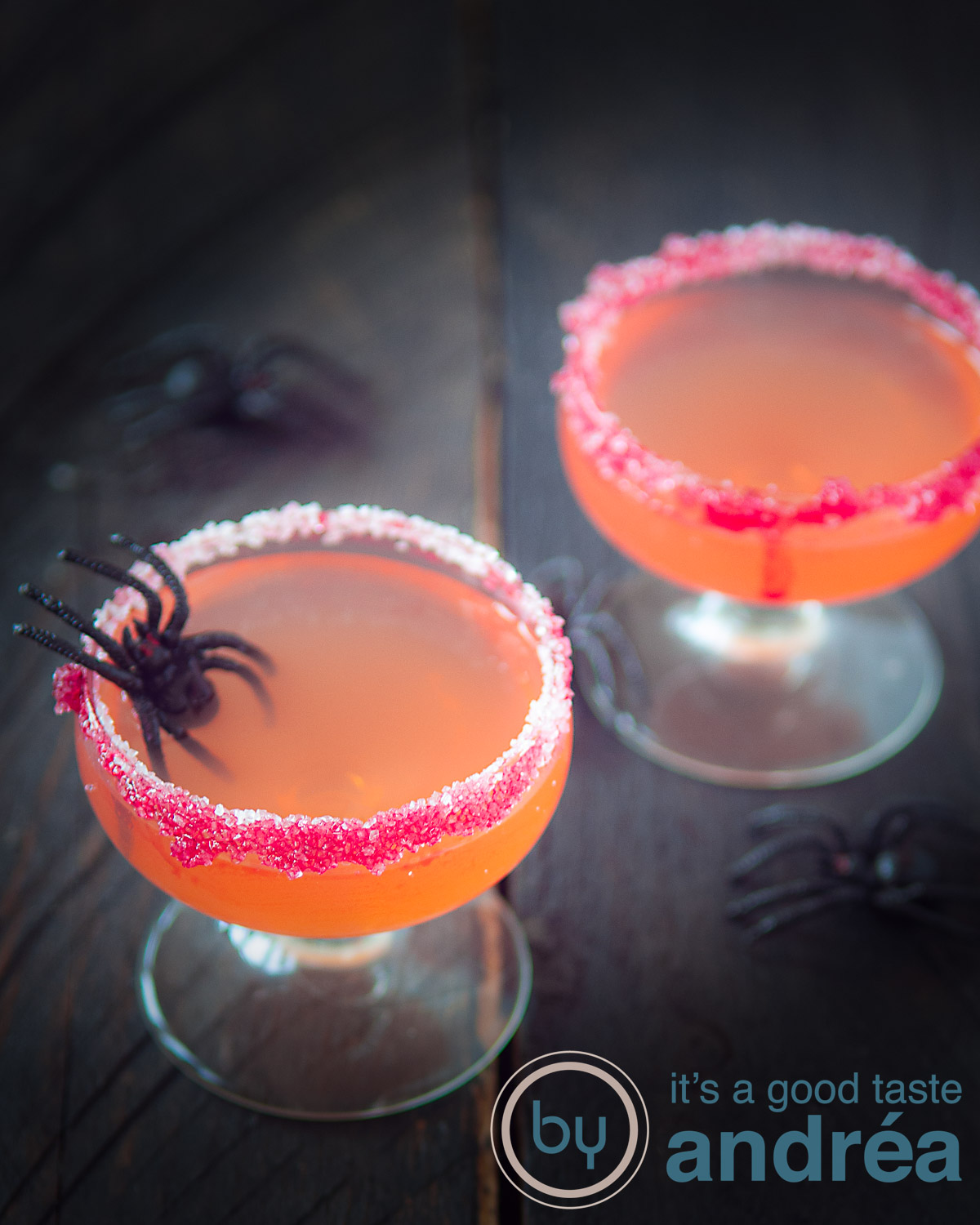 Twee Halloween cosmopolitan cocktails achter elkaar met spinnen op de tafel op een donkere ondergrond