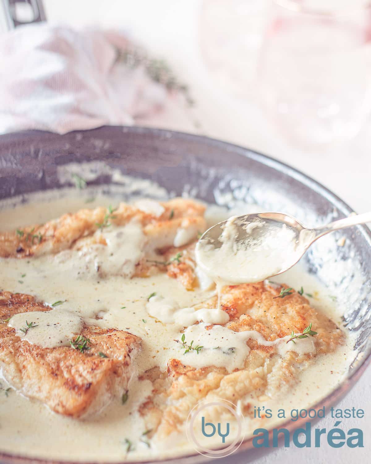 Een hoogtefoto van een koekenpan met kabejauwfilets die worden besprenkeld met witte wijn saus. Een witte ondergrond.