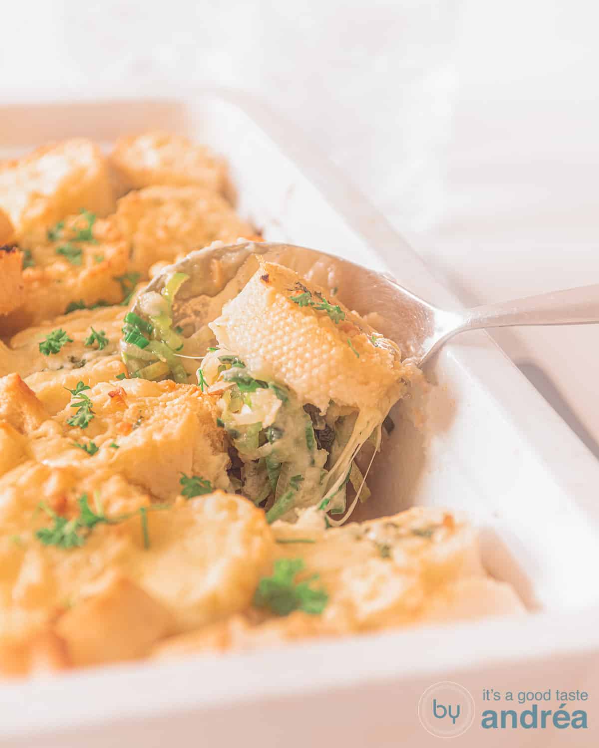 kip prei ovenschotel in een witte ovenschaal, een lepel schept een hap eruit.
