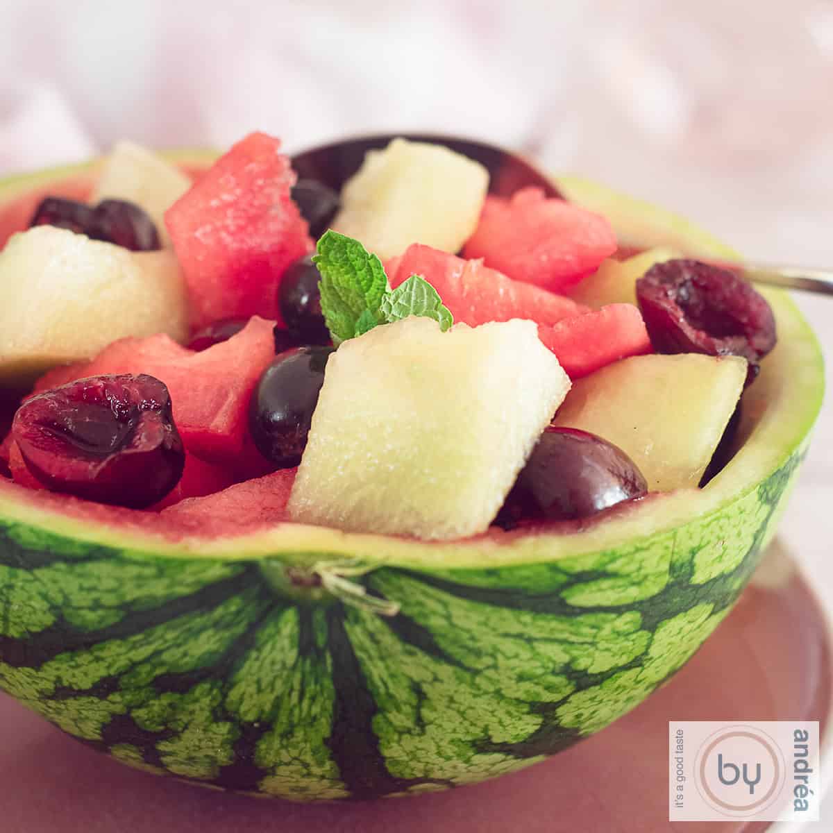 A square picture of a watermelon halfed and filled with fruit