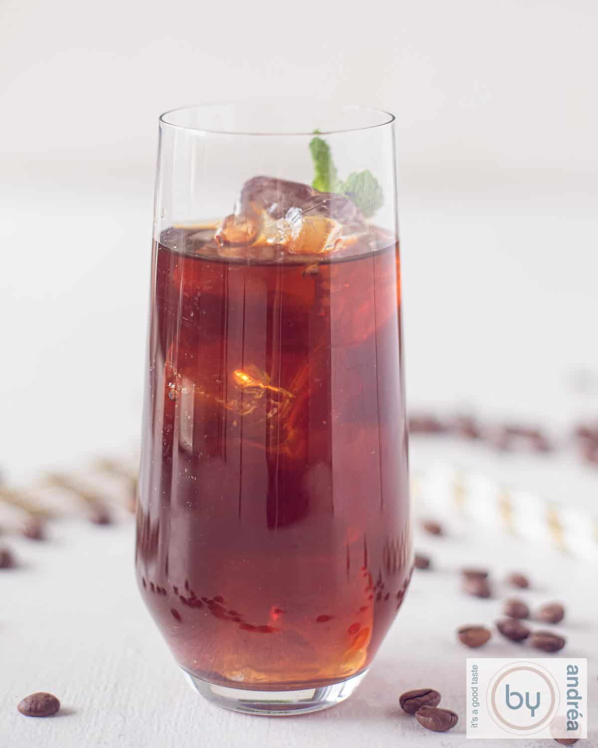 Een glas gevuld met Mexicaanse ijskoffie op een witte ondergrond. Rietjes en koffiebonen om het glas