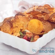 Een witte ovenschotel in Halloween stijl gevuld met kip, boontjes, tomaat en afgedekt met nacho chips en tortilla en kaas in een vierkante foto