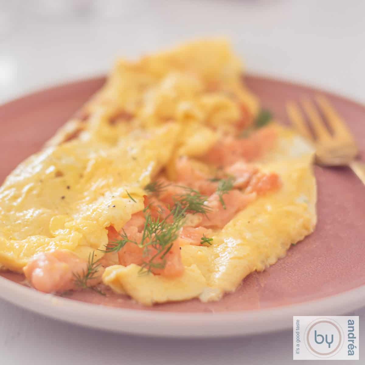 Een vierkante foto met een omelet gevuld met gerookte zalm en bieslook op een roze bord.