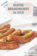 Braadworsten met biersaus en garnering van peterselie op een wit bakpapier. Een tekstoverlay bovenin duitse braadworst in bier, avondeten, makkelijk recept, comfort food