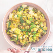 Een vierkante foto met gewokte prei op smaak gebracht met curry en chilivlokken. Een witte ondergrond.