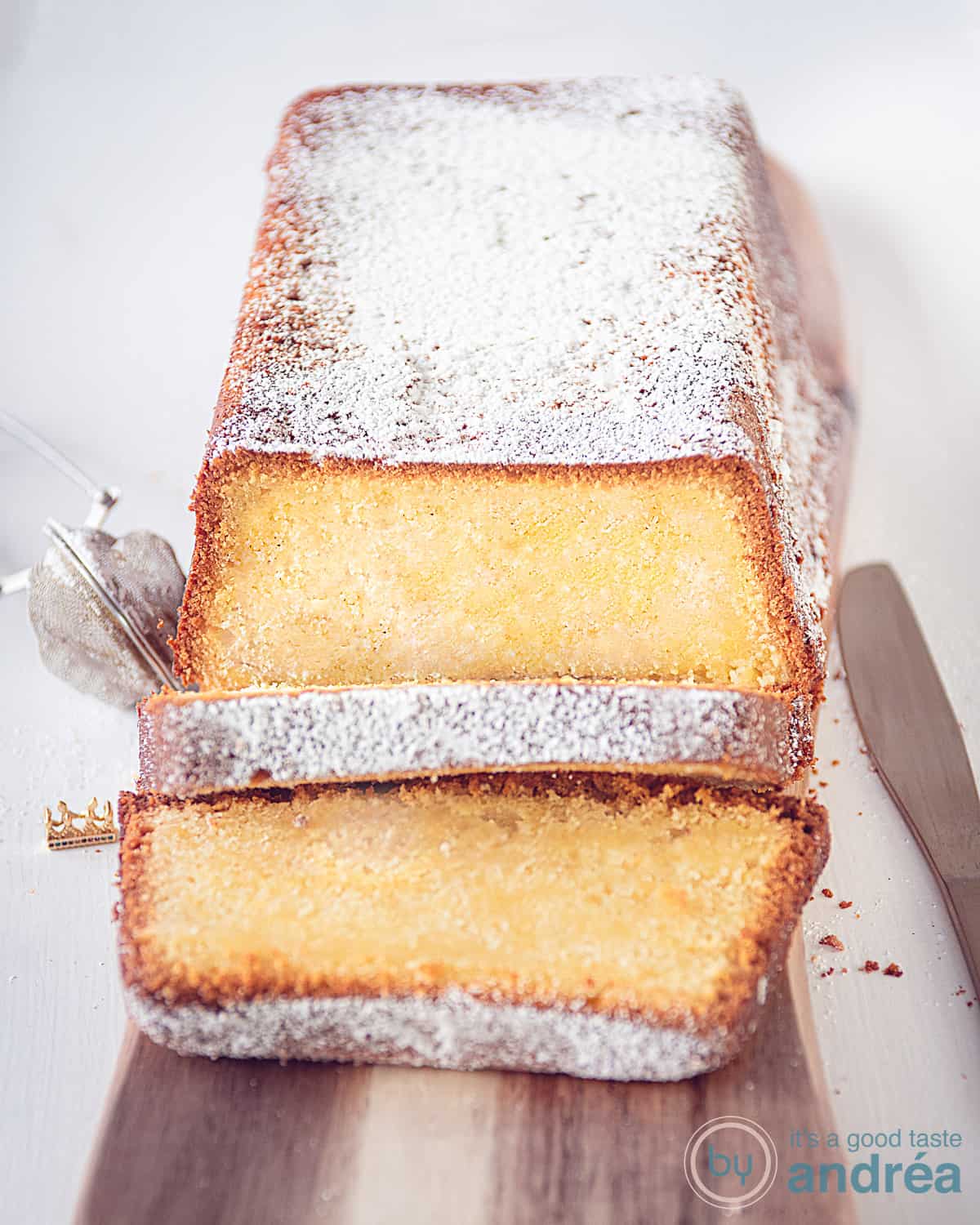 cream cheese pound cake on a wooden board on a white surface. Sprinkled with powdered sugar. Two slices cut off, lie in front of it.