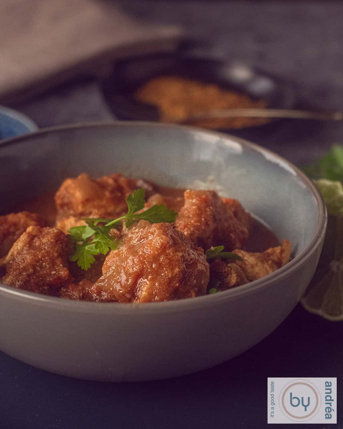 Een hoogtefoto met een roze schaal gevuld met kruidige curry met kip in een heerlijke saus. Een witte achtergrond met een roze witte theedoek.