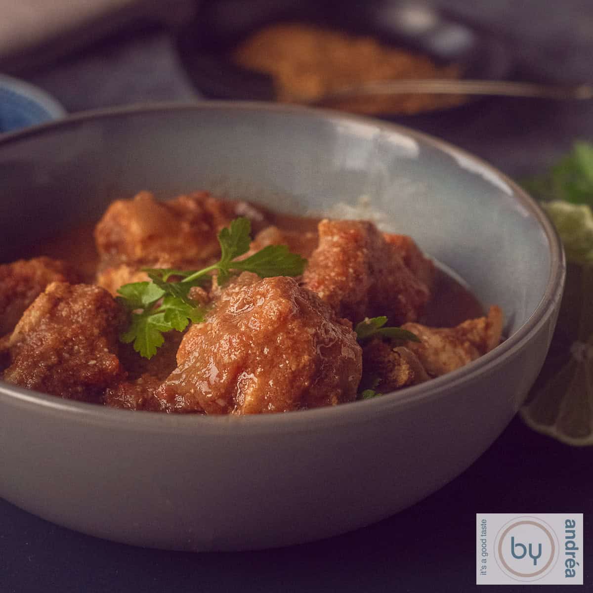 A square photo with a pink bowl filled with chicken curry with coconut and delicious herbs. A white background.