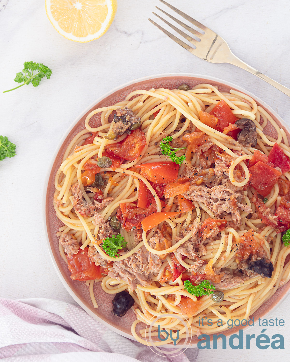 Een foto van bovenaf van spaghetti met een rijke tomatensaus (Puttanesca). Een gouden vork prikt in het bord. Een witte ondergrond.