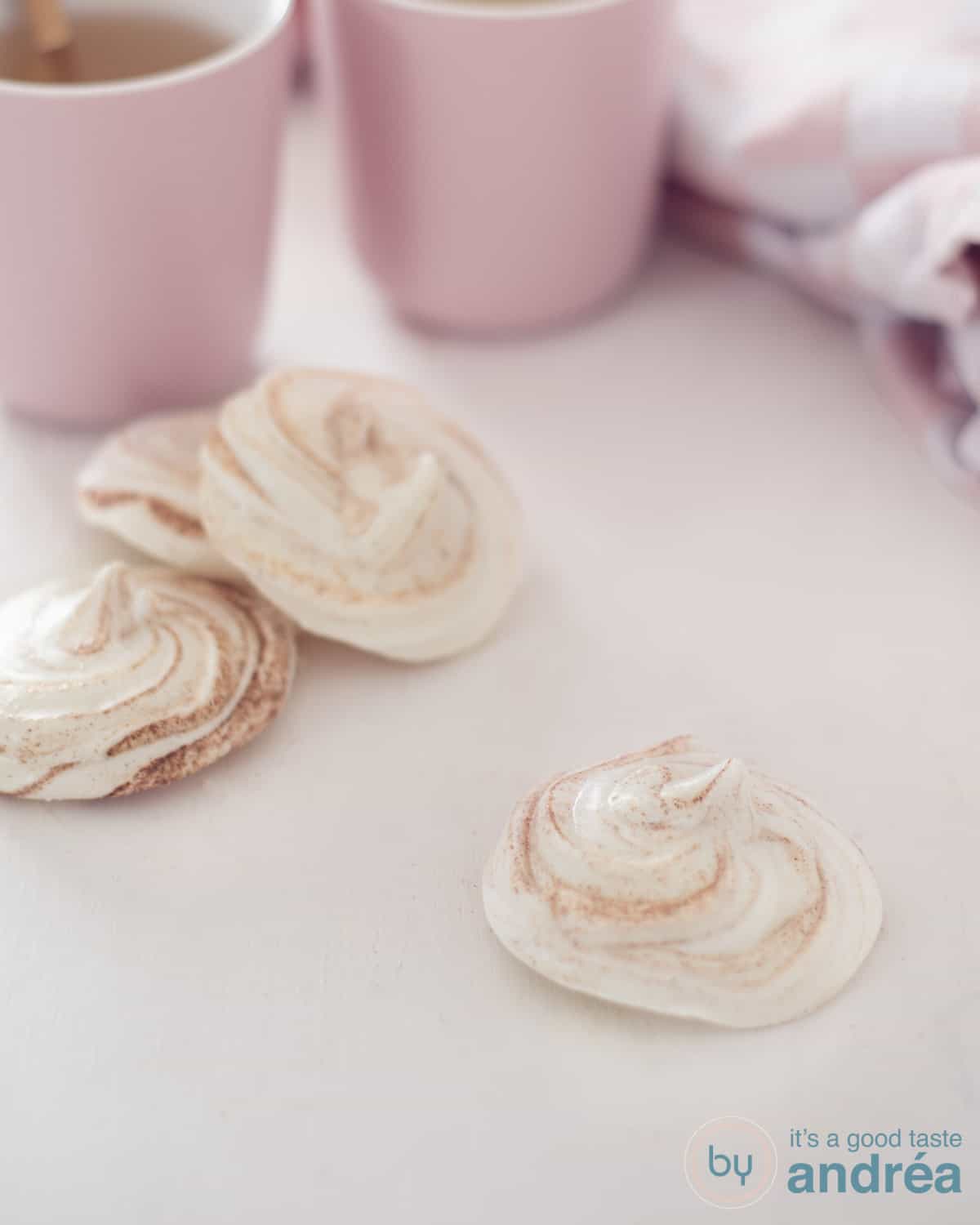 Een hoogtefoto met drie speculaas schuimpjes op een witte ondergrond. In de achtergrond twee roze mokken.