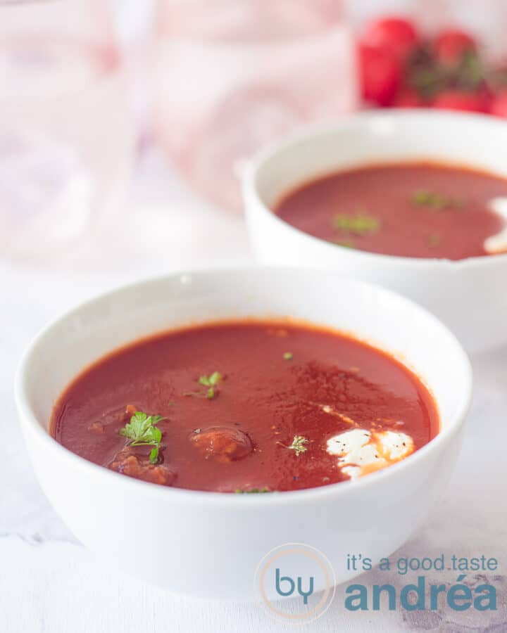 Twee kommen met tomatensoep met balletjes, room en verse peterselie. Twee lepels in de achtergrond.