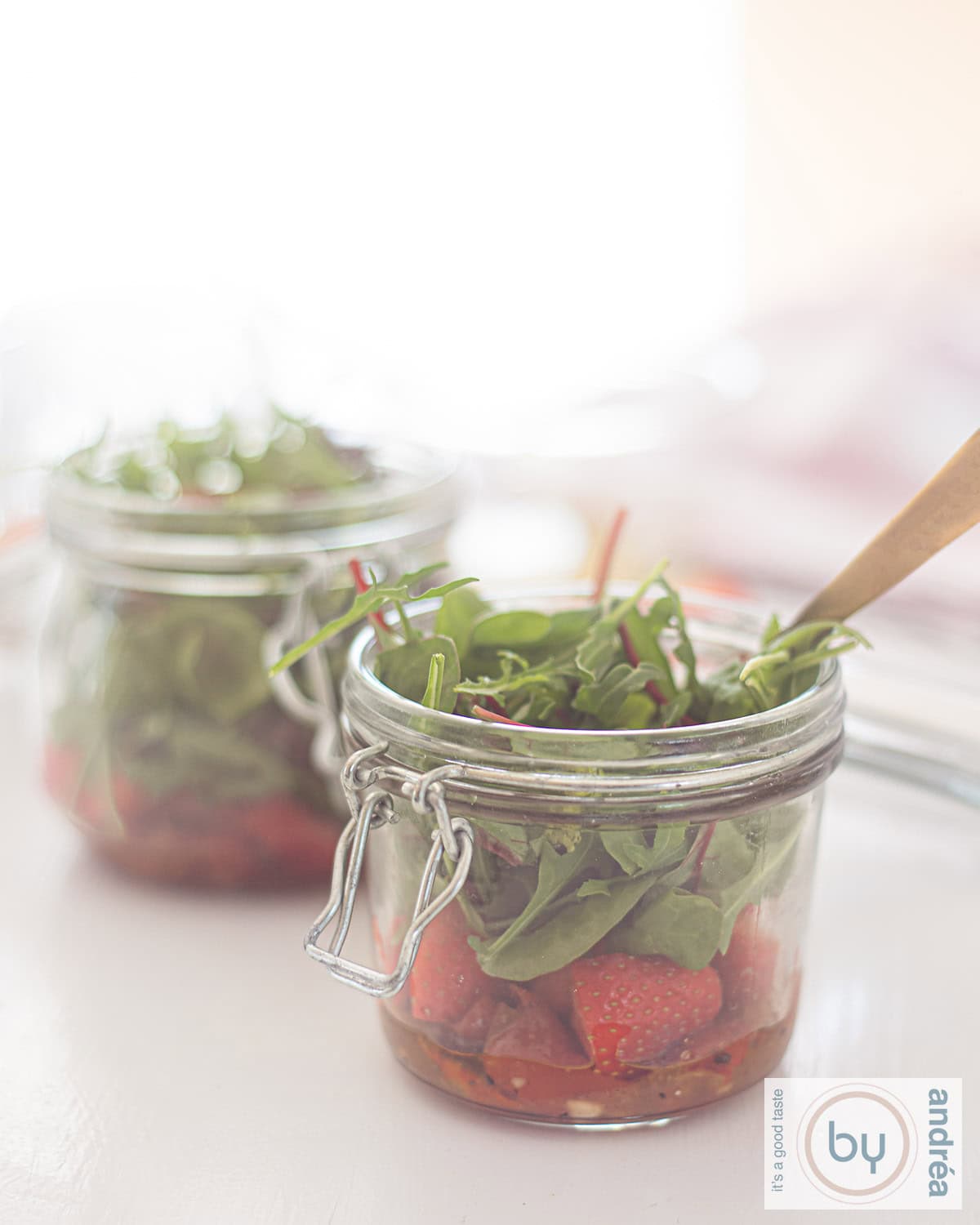 twee potjes met een groene salade, zongedroogde tomaten, aardbeien en een honing-mosterddressing