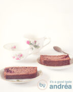 frambozen chocolade cake, twee plakjes op een bordje met bloemen. Een witte ondergrond. Linksachter in de achtergrond twee kopjes