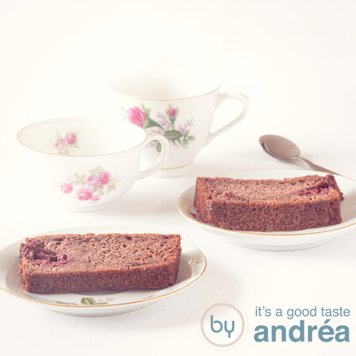 Een vierkante foto met twee bordjes met chocolade frambozen cake. Twee kopjes staan er links schuin achter
