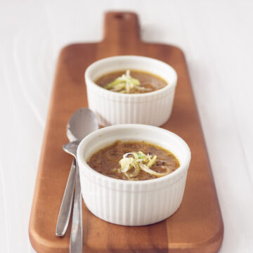 vegetarische prei kool soep in twee witte kommen op een houten plank. Een witte achtergrond