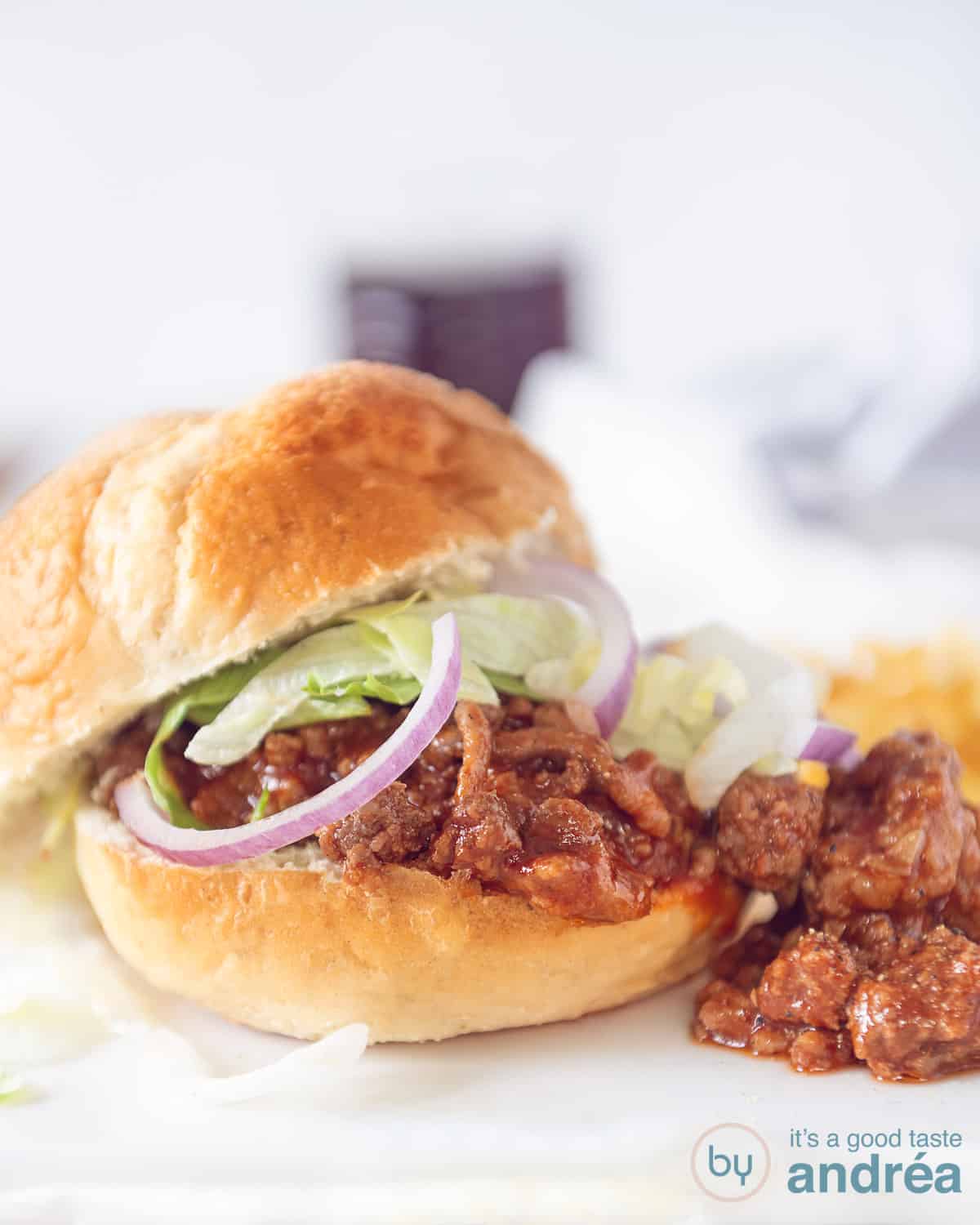 Sloppy Joe uit de slowcooker op een broodje op een witte ondergrond. Een topping van rode ui en sla.