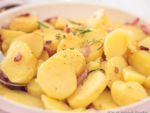 Een vierkante foto van een koekenpan met gebakken aardappels, rozemarijn, uitjes en spekjes. een witte achtergrond.