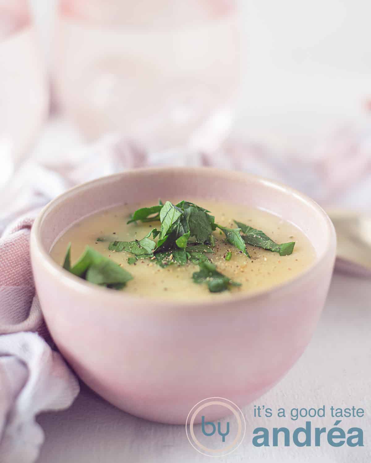 Een hoogtefoto van een roze bakje met kaas saus met parmezaan, knoflook en peterselie. In de achtergrond een roze witte theedoek en twee roze glazen op een witte ondergrond.