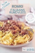 Een roze bord met pasta, rundvlees en saus, italian style. Een textoverlay bovenin: romig itlaiaans stoofvlees, slowcooker, makkelijk recept, wereldkeuken