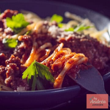 Een vierkante foto met een bord spaghetti met bolognese saus erdoor.
