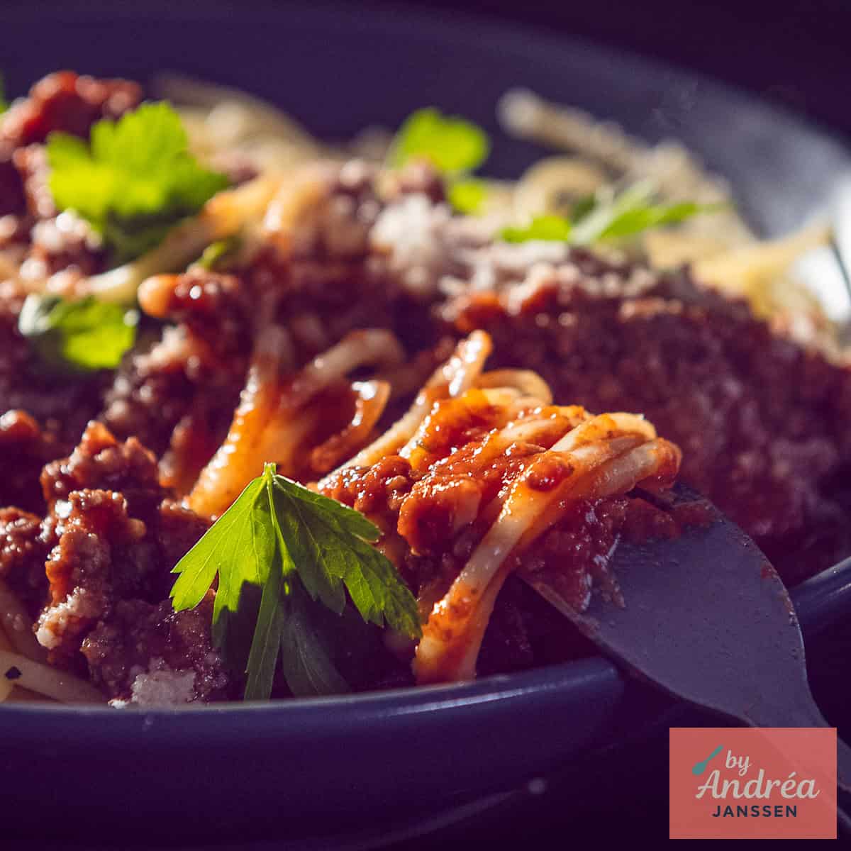 Een vierkante foto met een bord spaghetti met bolognese saus erdoor.