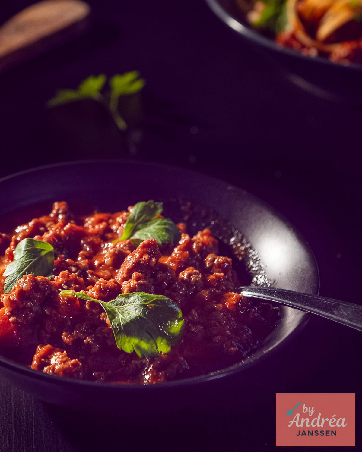 Een zwart schaaltje met bolognese saus met een garnering van peterselie