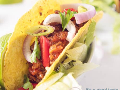 Een taco gevuld met chili zonder bonen. Met een topping van uien en peterselie op een witte achtergrond
