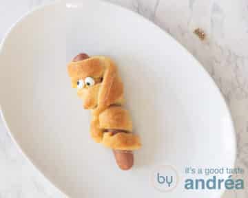 Een hotdog mummie op een wit bord op een witte ondergrond