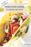 Een taco gevuld met chili con carne zonder bonen met een topping van ui, tomaat en peterselie. Een tekst bovenin: Chili con carne zonder bonen, makkelijk recept, slowcooker