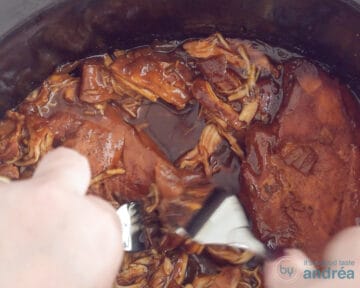 Een slowcooker waarin de kip door twee vorken uit elkaar wordt getrokken