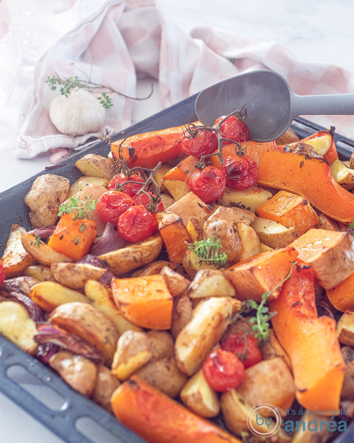 Een deel van een ovenplaat met geroosterde tomaatjes, ui, pompoen en aardappeltjes. Alles op smaak gebracht met tijm.