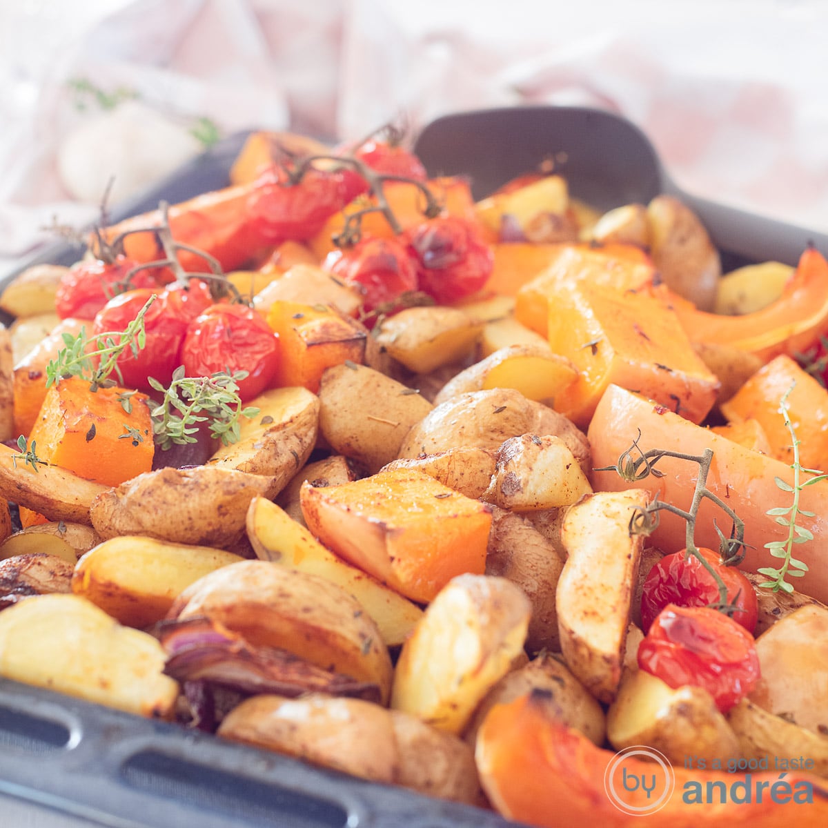 Een vierkante foto met een bakplaat met pompoen, cherry tomaten, aardappels en ui. Tijm brengt alles op smaak.