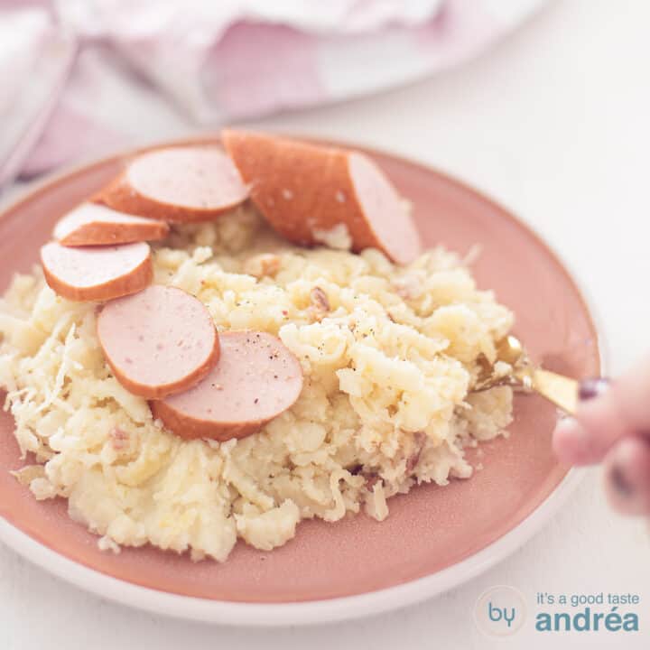 A square photo with a pink plate with sauerkraut stew with smoked sausage