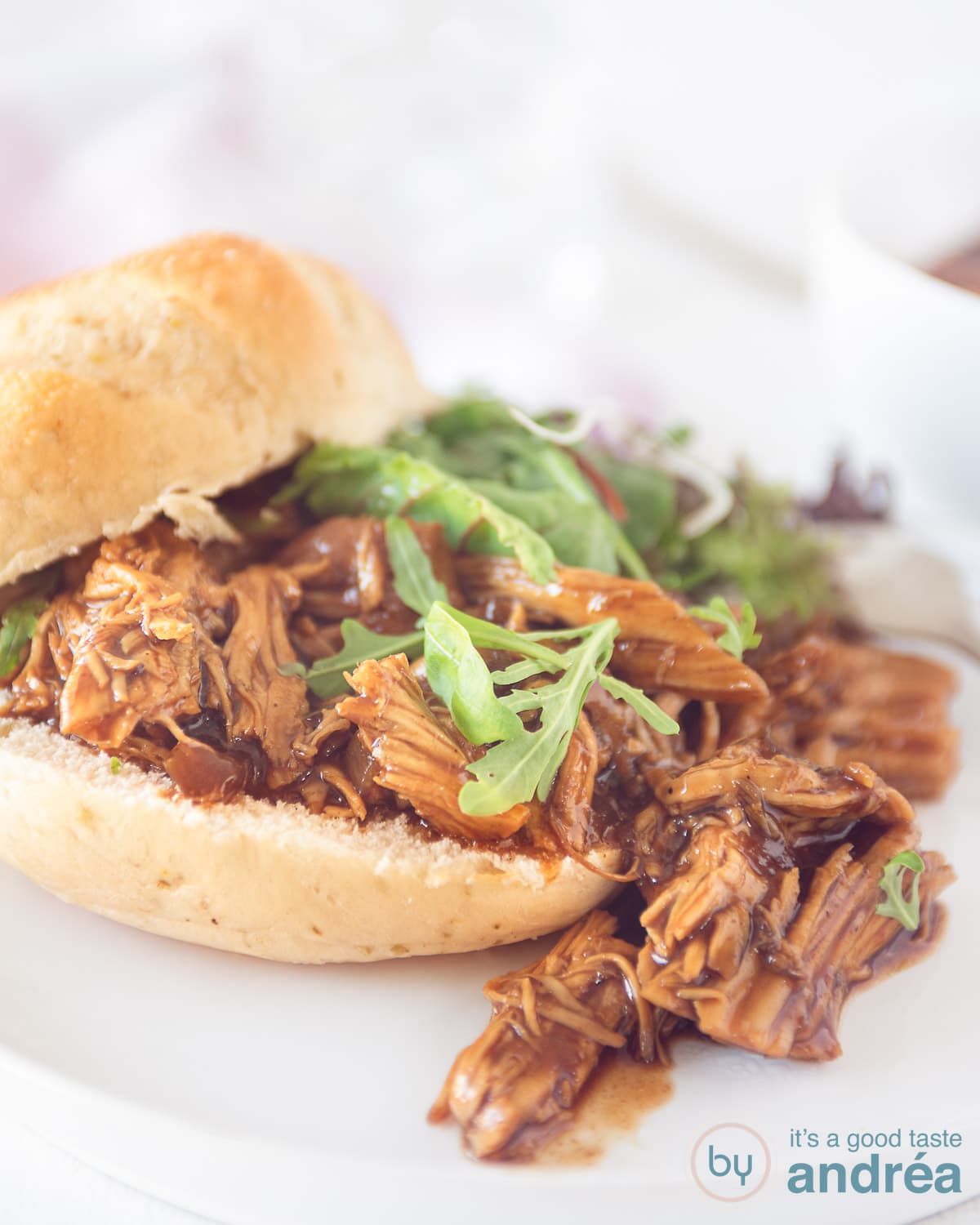 Een hoogtefoto met een broodje pulled chicken met daarop salade. Een witte achtergrond.