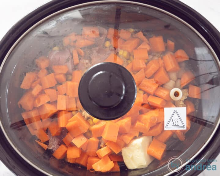 Een slowcooker gevuld met alle ingrediënten voor een Brunswick stew met een deksel erop.