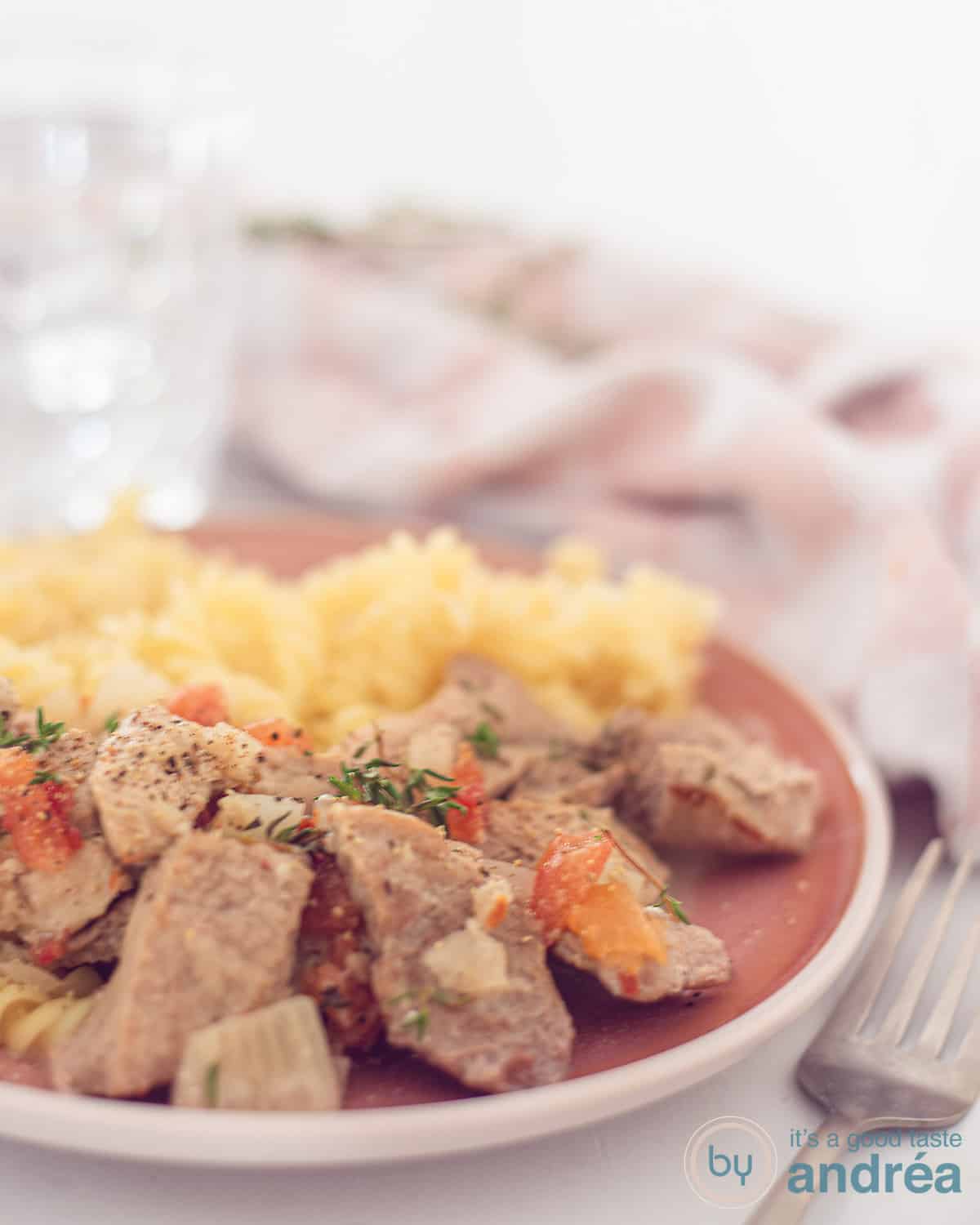 Een hoogtefoto met malse hamlappen met een romige saus en pasta op een roze bord. In de achtergrond een roze witte theedoek.