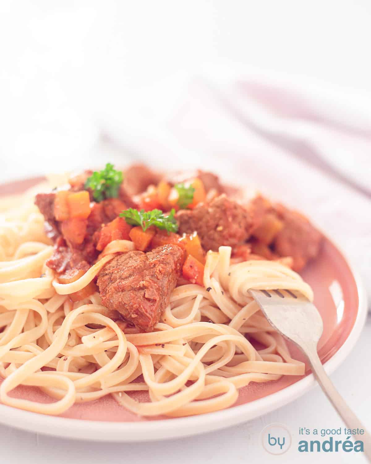 Een hoogtefoto met Spezzatino de Manzo op een bedje van tagliatelle. Gemaakt in de slowcooker. Een witte ondergrond.