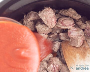 In de slowcooker wordt over de vleesmix de gezeefde tomaten gegoten