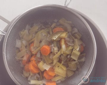 A sieved pot of chicken soup, with a sieve of leftover vegetables on top.