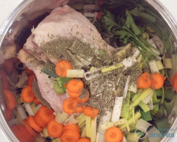 A pan filled with chicken legs, herbs and fresh vegetables.