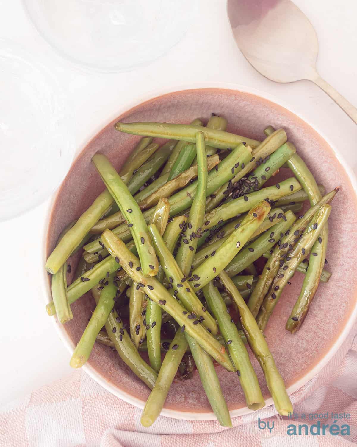 Een foto van bovenaf van een roze schaal gevuld met gesmoorde boontjes in een Oosterse saus op een witte ondergrond.