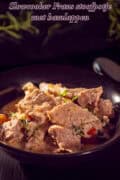 Een zwarte schaal met blokjes ham in een romige saus met kruiden en wijn. Een tekst bovenin: Slowcooker Frans stoofpotje met hamlappen